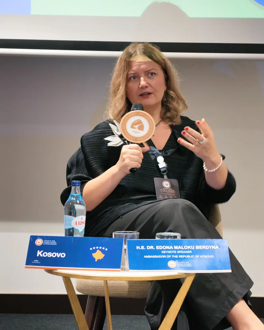 The Ambassador of Kosovo speaking from an armchair on stage, behind her keynote speaker name plate
