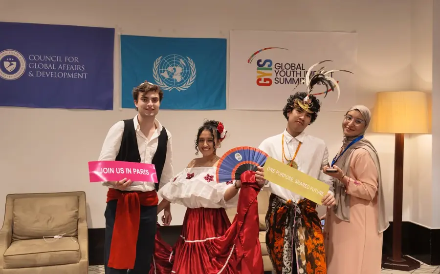 Four delegates, three in national dress, holding a Join us in Paris placard under CGAD, UN and GYIS banners